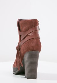 Stivale alla caviglia in suede marrone con tacco robusto, dotato di fasce di pelle incrociate e zip laterale. Suola in gomma testurizzata per una migliore aderenza.