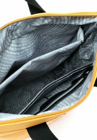 Wnętrze żółtej torby na ramię z szarą podszewką ozdobioną wzorem tekstowym, podzielone przegrody oraz zapinana na zamek kieszeń dla lepszej organizacji.