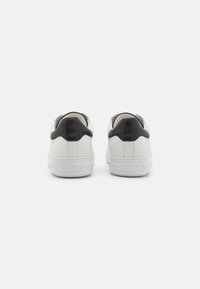 White leather sneakers with a black leather heel accent, textured sole, and smooth finish. Rounded shape with minimal design details.