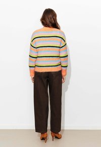 Pull rayé et duveteux aux couleurs pastel (rose, bleu, vert) avec des accents noirs, associé à un pantalon large marron et des talons hauts marron.