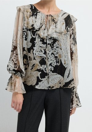 Transparente Langarmbluse mit schwarzem, beigem und weißem verziertem Blumenmuster, gerafftem Kragen und Manschetten, kombiniert mit dunkler Nadelstreifenhose.