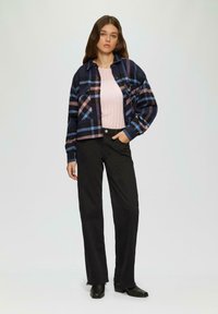 Geruite blazer in marineblauw, roze en blauw, gedragen over een lichtroze geribd sweater, gecombineerd met zwarte rechte broek en zwarte enkellaarsjes.