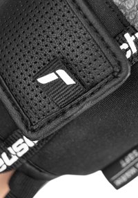 Supporto per polso atletico nero con tessuto traspirante e perforato, cinturino regolabile e superficie texturizzata con dettaglio del marchio.