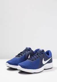 Zapatillas deportivas de malla azul con detalles y logo en blanco. Punta redondeada, suela acolchada y parte superior con patrón para mayor transpirabilidad y comodidad.