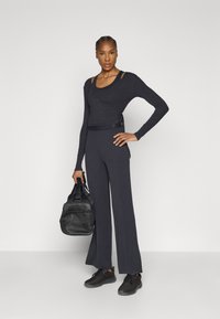 Fekete, hosszú ujjú felső, átkötős dizájnnal és oldalt megkötős részlettel, fekete, bővülő szárú nadrággal párosítva. Kiegészítők közé tartozik egy fekete edzőtáska és sportcipők.