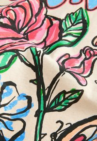 Primo piano di tessuto floreale colorato con fiori rosa e blu, foglie verdi e contorni neri disegnati a mano su sfondo beige.