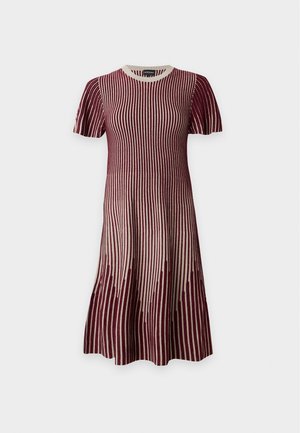 Femme aux longs cheveux foncés portant une robe rayée marron et beige, tenant un sac tissé couleur tan avec des poignées en cuir et des ballerines roses.