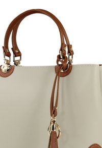 Sac à main beige en matériau synthétique lisse, avec poignées en cuir marron, accessoires dorés et accents décoratifs noués.