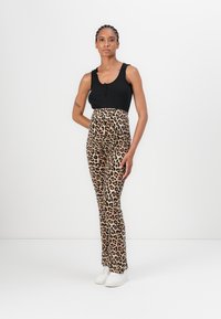Crni rebrasti top na bretelama s dugmadima uparen s tajicama visokog struka u bež i crnom leopard uzorku, završeno s bijelim tenisicama.
