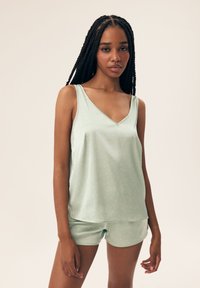 Jasnozielony komplet do spania składający się z bezrękawowego topu z dekoltem w serek w białe kropki oraz pasujących szortów, wykonany z gładkiego materiału.