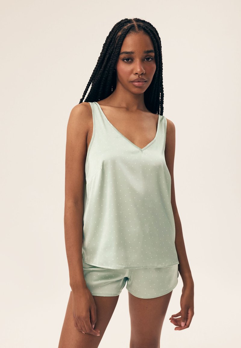 Jasnozielony komplet do spania składający się z bezrękawowego topu z dekoltem w serek w białe kropki oraz pasujących szortów, wykonany z gładkiego materiału.