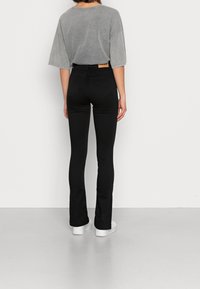 Černé rozšířené džíny s zadními kapsami, vysokým pasem a béžovou koženou nášivkou. V kombinaci s krátkým šedým oversize tričkem. Bílá platformová obuv.