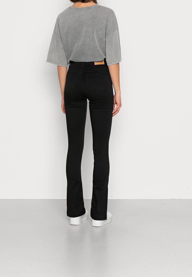 Černé rozšířené džíny s zadními kapsami, vysokým pasem a béžovou koženou nášivkou. V kombinaci s krátkým šedým oversize tričkem. Bílá platformová obuv.