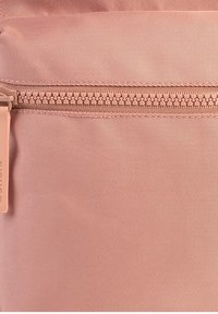 Pochette en tissu rose clair avec une texture lisse, dotée d'une fermeture éclair sur le dessus et d'une tirette de fermeture éclair de marque. Motif à côtes horizontal visible.