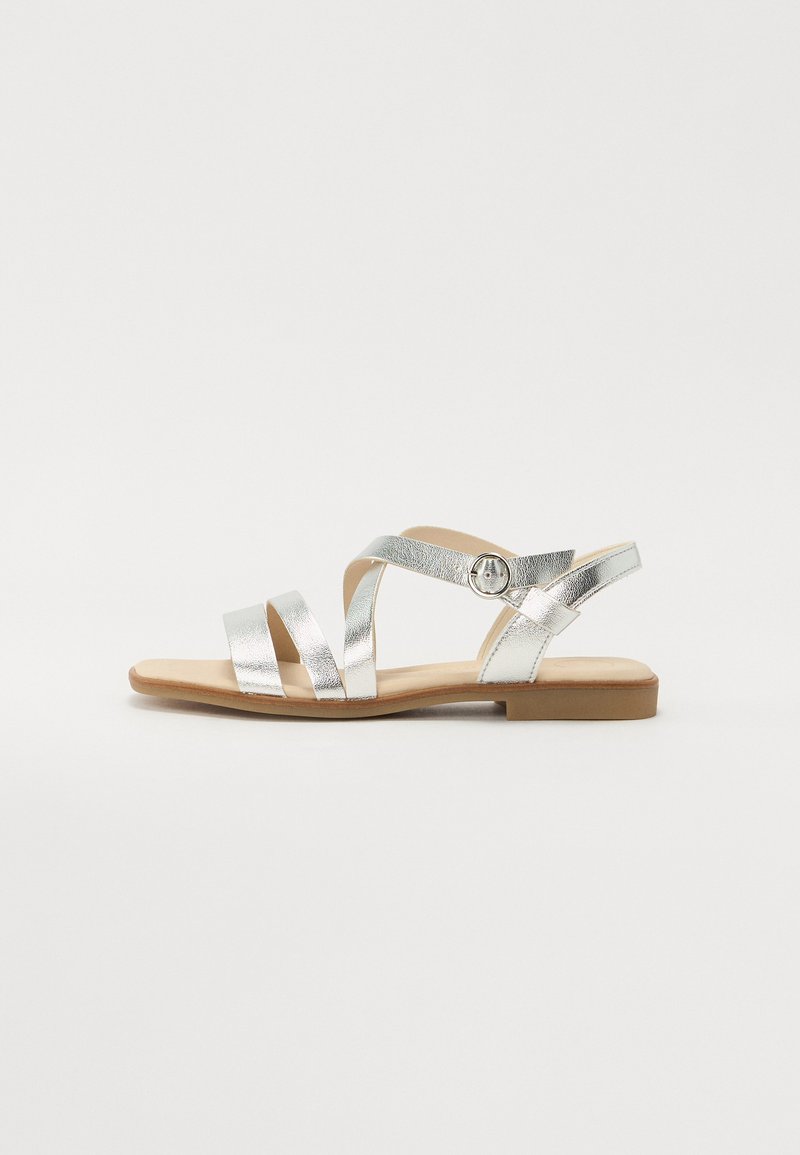 Silberne metallische flache Sandalen mit kreuzenden Riemen, Schnallen-Detail und einem braunen Fußbett. Sie verfügen über ein minimalistisches Design und eine glatte Oberfläche.