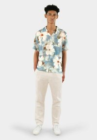 Kortärmad blå blommig skjorta med vita blommor, kombinerad med ljusbeiga byxor och vita sneakers. Skjortan har krage och knäppning framtill.