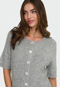 Cardigan en tricot gris à manches courtes, col rond, et cinq boutons blancs sur le devant. Texture douce et coupe décontractée.