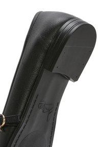 Zapato negro con punta redondeada, parte superior de cuero texturizado y suela de goma plana con diseño grabado y detalles de costura.