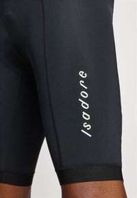 Shorts de vélo noirs en matériau extensible, dotés de coutures plates et d'un logo "Isadore" blanc bien visible sur le côté.
