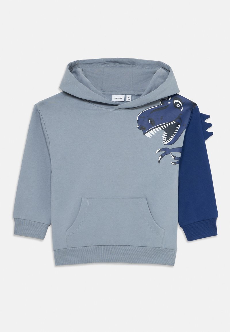 Felpa per bambini di colore blu chiaro con una grafica di un dinosauro blu scuro sulla spalla e punte di tessuto tridimensionale su una manica.