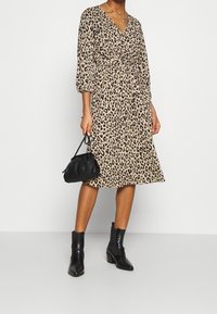 Šaty s leopardím vzorem, výstřihem do V, tříčtvrtečními rukávy a vázáním v pase. Kombinováno s černými kotníkovými botami a malou černou kabelkou.