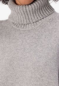 Suéter gris de cuello alto con textura acanalada, que presenta un alto cuello y material de punto suave y grueso. Vista cercana de la tela.