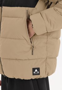 Beige vadderad jacka med svarta detaljer, utrustad med en dragkedjefick, texturerad yta och en svart logopatch på den nedre fållen.