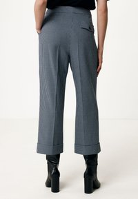 Pantaloni a righe, a vita alta, in blu e bianco, con gambe larghe, risvolti e una tasca sul retro. Abbinati a stivali neri con tacco.