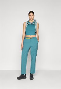 Tiefblaue ärmellose Bluse mit cropped Design und passenden Cargo-Hosen. Das Outfit verfügt über gelbe Gürtelakzente und graue Wanderschuhe.