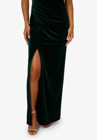Zelené sametové maxi šaty s řaseným designem a rozparkem až po stehna. Mají hladkou texturu a nastavitelné špagetové ramínka.