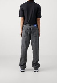 Svart t-shirt i kombination med mörkgrå denimjeans. Jeansen har en blå logopatch på midjebandet och en lös passform.