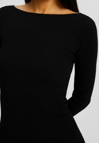 Robe noire à manches longues côtelées, présentant un large décolleté bateau et une silhouette ajustée, mettant en valeur une texture lisse.