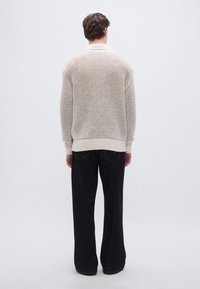 Πλεκτή ζακέτα σε εκρού χρώμα με υφή, με ριμπ γιακά και μανσέτες, συνδυασμένη με άνετα σκούρα τζιν.