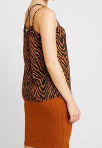 Top senza maniche a stampa zebra arancione e nera con spalline sottili, caratterizzato da una vestibilità comoda e da un tessuto leggero. Abbinato a una gonna a coste color ruggine.