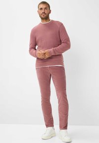 Rosa gerippter Strickpulli kombiniert mit rosa Cordhosen und weißen Sneakers. Der Pulli hat einen Rundhalsausschnitt und lange Ärmel.
