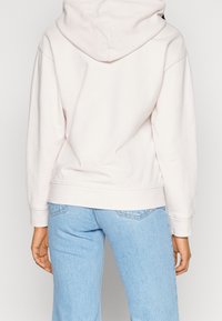 Haut à capuche rose clair, fabriqué en tissu doux. Présente une coupe décontractée et des poignets côtelés, associé à un jean bleu clair.