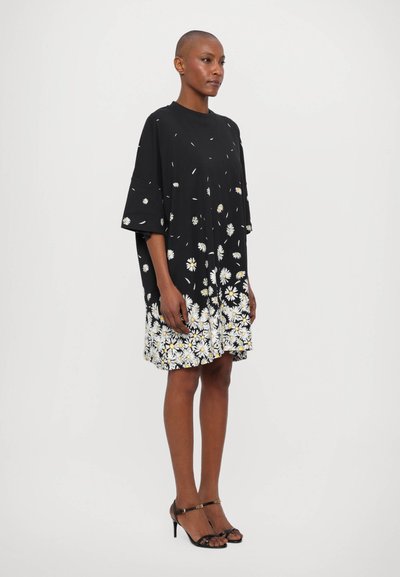 Overdimensioneret sort kjole med blomsterprint, der har margueritter i kanten. Lavet af blødt stof, med brede ærmer og en afslappet pasform.