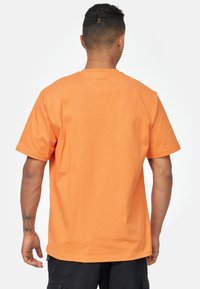 Kortärmad orange bomulls-t-shirt med en klassisk passform, slät textur och rakt nederkant, visad från en bakvy.