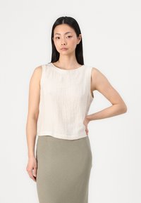 Top senza maniche in lino beige con scollatura rotonda, caratterizzato da una vestibilità rilassata e un orlo leggermente accorciato, abbinato a una gonna verde oliva strutturata.
