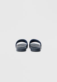 Φλατ σανδάλια σε ναυτικό μπλε με μινιμαλιστικό σχεδιασμό, που διαθέτουν δύο φαρδιές λουριά και υφασμένο πέλμα για καλύτερη πρόσφυση, στηριζόμενα σε σταθερή βάση.