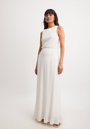Robe maxi blanche sans manches avec un design texturé et plissé, dotée d'une taille cintrée. Elle présente un col rond et une jupe fluide traînant au sol.