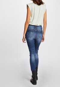 Top corto de manga corta verde claro combinado con jeans ajustados azul oscuro. Los jeans cuentan con bolsillos traseros con detalles de costura, una textura envejecida y piernas ajustadas.
