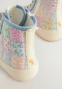 Høje sneakers med patchwork blomsterstof, lyseblå kant, cremefarvet sål og en lille gul blomst detalje på bagtil.