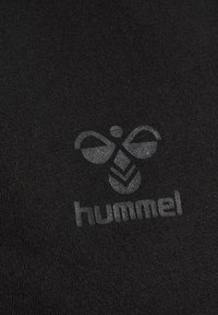 Sort t-shirt stof med et subtilt, reflekterende logodesign, der inkluderer et bi-motiv og brandnavnet "hummel" i grå.