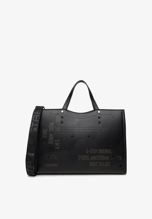 Černá taška na rameno s dvojitými uchy a značkovým ramenním popruhem, na kterém je vyražený text včetně "G-Star Original" a "Studio Amsterdam".