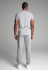 Lys grå atletisk outfit med en tætsiddende T-shirt og tætsiddende sweatpants, lavet af blødt stof med subtil glans og detaljer i siden.