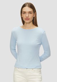 Chemise à manches longues bleu clair avec un col rond et une texture douce, associée à un pantalon blanc. Design simple, sans motifs ni éléments métalliques visibles.