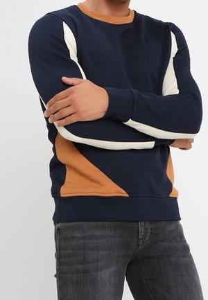 Marineblaues Sweatshirt mit cremefarbener und beigefarbener Blockierung, langen Ärmeln, Rundhalsausschnitt und lockerem Schnitt. Glatte Stofftextur, keine sichtbaren Beschläge.