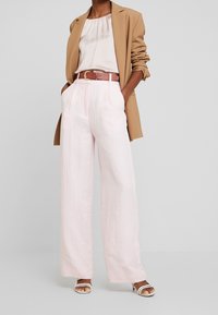 Beige Blazer über einer hellrosa Bluse, kombiniert mit weiten hellrosa Hosen und einem braunen Gürtel. Weiße Sandalen mit Riemchen runden das Outfit ab.