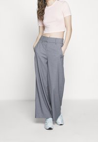 Ljust rosa, croppad t-shirt med korta ärmar och en liten vit logotyp. Grå, vida byxor med ränder, med framfickor. Ljusblå sneakers.